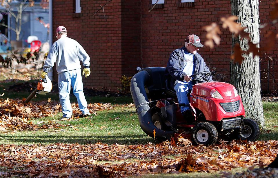 Thom Watson uses a leaf blower to clear the leaves the yard as his father, Dave Watson picks them up using the garden tractor on Center Lane Drive in Ashland on Friday, Nov. 12, 2021.