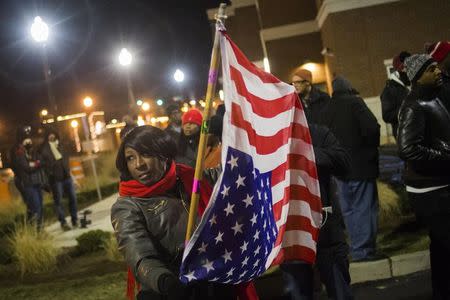 A protester, who was among dozens demanding the criminal indictment of a white police officer who shot dead an unarmed black teenager in August, holds a U.S. flag outside the Ferguson Police Station in Missouri November 20, 2014. REUTERS/Adrees Latif