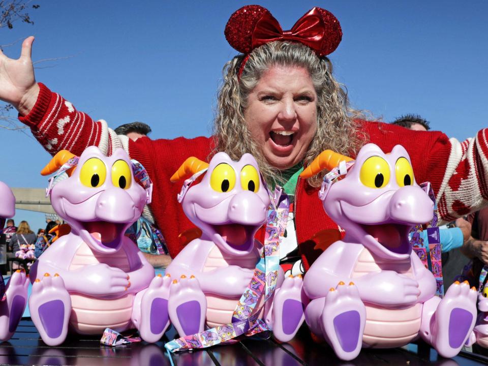 A woman with Minnie Mouse ears on smiling behind purple smiling and sitting plastic dinosaur figures.