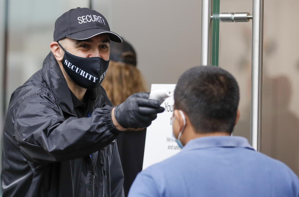 A security guard takes the temperature of a customer at a shopping precinct in Sydney, Australia, Sunday, Jan. 3, 2021. Masks have been made mandatory in shopping centers, on public transport, in entertainment venues such as a cinema, and fines will come into effect on Monday as the state government responds to the COVID-19 outbreak on Sydney's northern beaches, which is suspected to have also caused new cases in neighboring Victoria state. (AP Photo/Mark Baker)