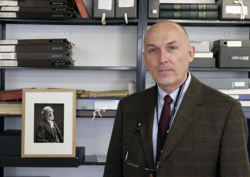 Jean-Charles Forgeret poses next to photograph of Eugene Emmanuel Viollet-le-Duc, the renowned architect who designed the spire that was added to the medieval cathedral in the 19th century, in Charenton le Pont, outside Paris, Thursday, April 18, 2019. The reconstruction of Paris' Notre Dame Cathedral will rely on part on extensive plans drawn up in the 19th century for its last big renovation. Forgeret noted that the last restoration took 20 years, and cast doubt on the French president's 5-year deadline on fixing Notre Dame this time. (AP Photo/Nicolas Garriga)