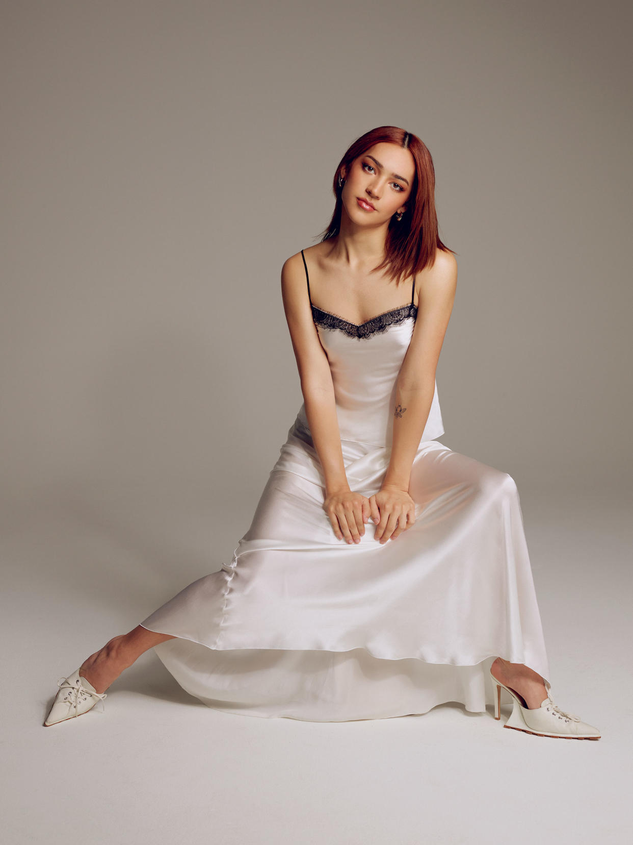 Miss Benny sits and poses for a portrait in a white silk dress with black lace trim and high heels