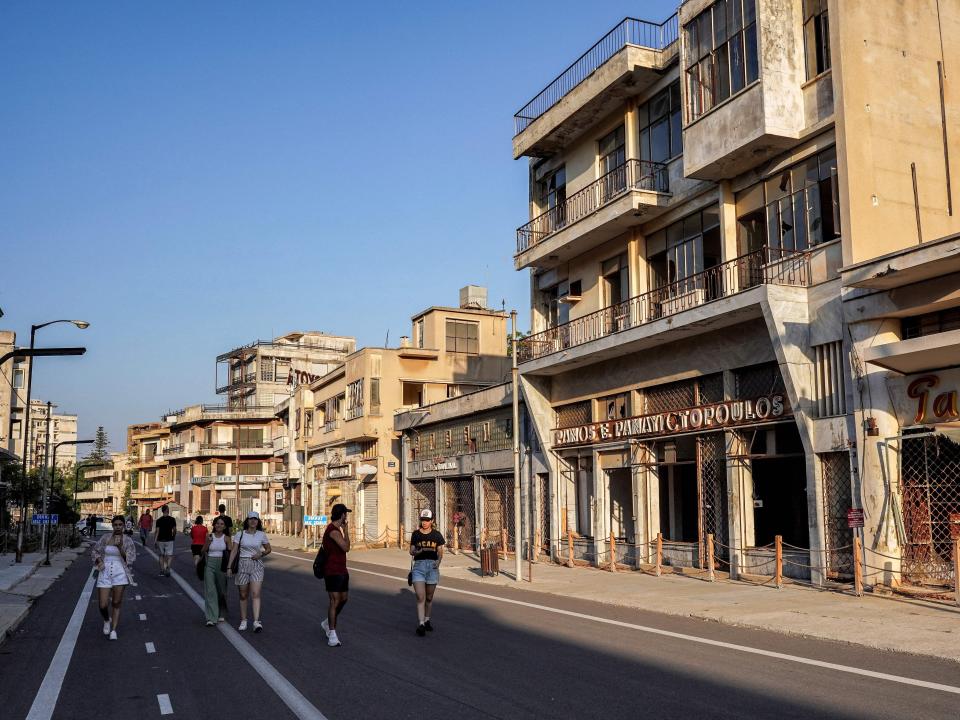 People walk past abandoned buildings along the path designated by Turkish forces for visitors in Varosha, in the fenced off area near Famagusta in the Turkish-controlled north of the divided eastern Mediterranean island of Cyprus, on September 18, 2022.