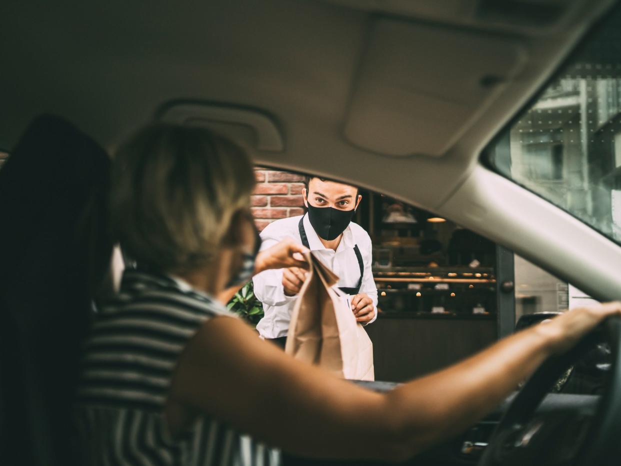 Waiter giving disposable package with food to pretty smiling female driver