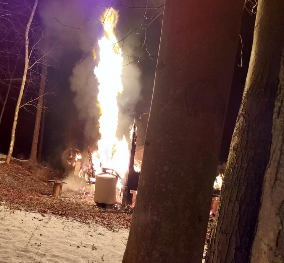 Flames erupt from a 150-gallon propane gas tank outside a Gunn Road home destroyed by fire early Friday morning. The blaze claimed the life of a dog and caused serious burns to a German Shepherd housed in a pen outside the cabin.