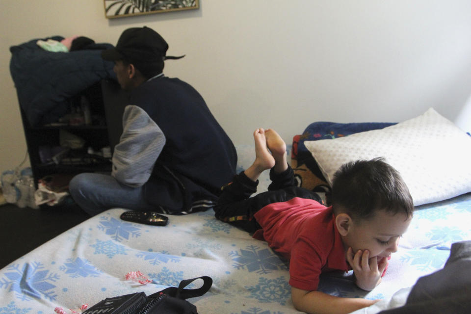 Four-year-old Fraiber Peraza looks at a phone while Franklin Peraza sits on an inflatable bed in their 'micro apartment' in Seattle on Monday, March 11, 2024. (AP Photo/Manuel Valdes)
