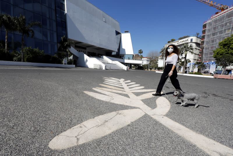 A woman wearing a protective face mask walks her dog past a Palme d'Or symbol on the pavement near the Festival palace on the Croisette in Cannes where the Cannes Film Festival and the Cannes Lions take place