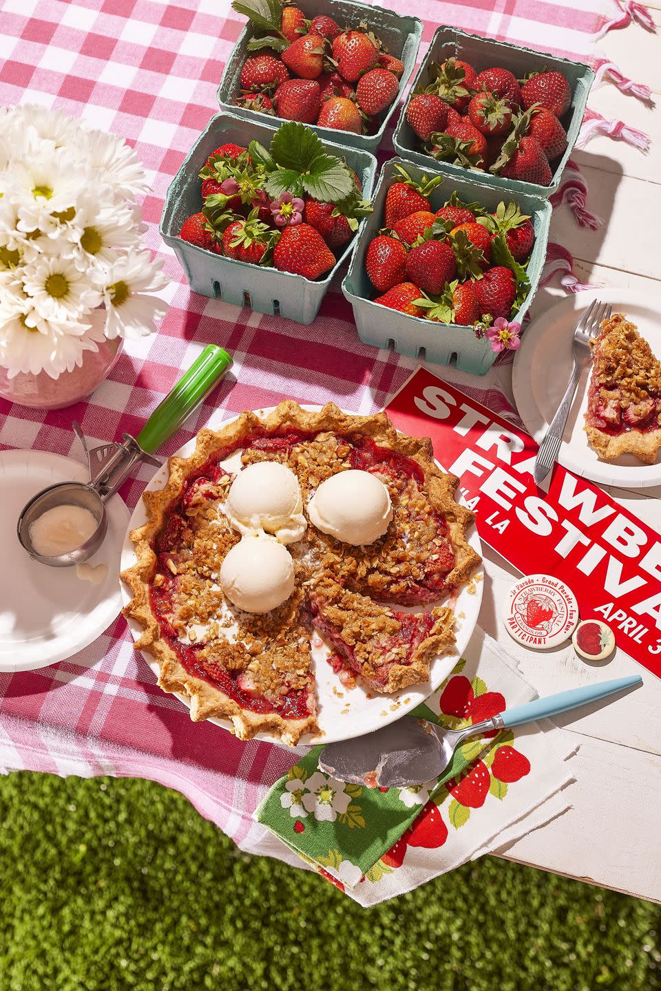 strawberry almond crumble pie in a white pie dish on a picnic table and topped with three scoops of vanilla ice cream