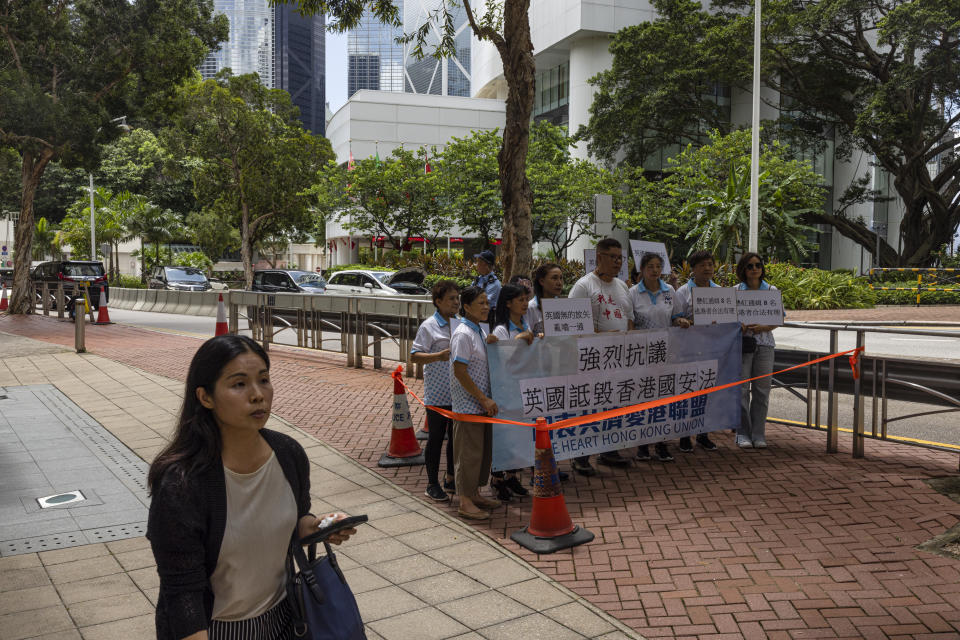 A pedestrian passes a pro-China group holding a mini protest with a banner reading: "Strong protest against the UK smearing Hong Kong National Security Law" after the British government criticised the arrest warrants issued for 8 pro-democracy activists living in the United States, Britain, Canada and Australia for alleged national security offenses in Hong Kong, Thursday, July 6, 2023. (AP Photo/Louise Delmotte)