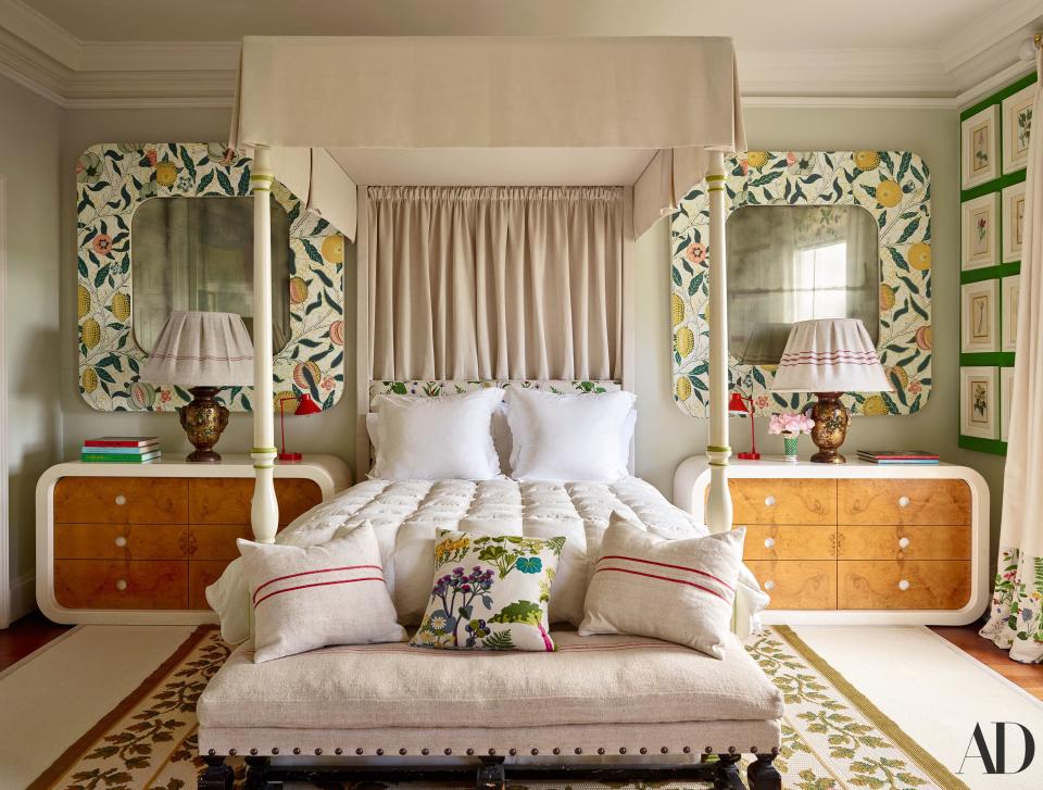 In a guest room, custom mirrors wrapped in wallpaper flank a linen-covered four-poster. Vintage chests, Japanese lamps, and needle-point rug.