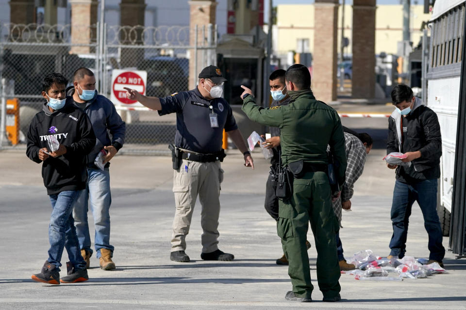 U.S. Customs and Border Protection officers, center, instruct migrants to walk toward the McAllen-Hidalgo International Bridge while deporting them to Mexico, Saturday, March 20, 2021, in Hidalgo, Texas. The fate of thousands of migrant families who have recently arrived at the Mexico border is being decided by a mysterious new system under President Joe Biden. U.S. authorities are releasing migrants with “acute vulnerabilities” and allowing them to pursue asylum. But it's not clear why some are considered vulnerable and not others. (AP Photo/Julio Cortez)