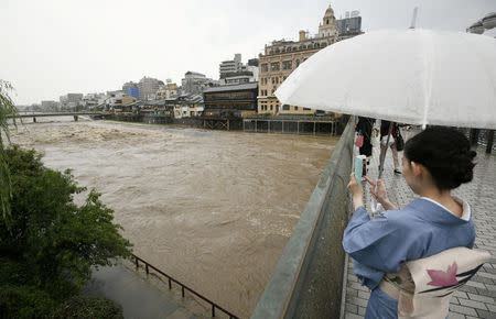 A kimono-clad woman using a smartphone takes photos of swollen Kamo River, caused by a heavy rain, from Shijo Bridge in Kyoto, western Japan, in this photo taken by Kyodo July 5, 2018. Mandatory credit Kyodo/via REUTERS ATTENTION EDITORS - THIS IMAGE WAS PROVIDED BY A THIRD PARTY. MANDATORY CREDIT. JAPAN OUT. NO COMMERCIAL OR EDITORIAL SALES IN JAPAN.