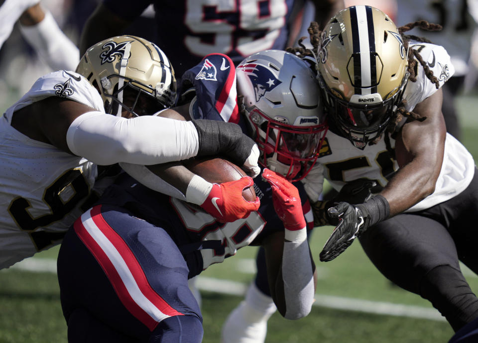 New England Patriots running back Rhamondre Stevenson, center, is brought down by New Orleans Saints defensive end Malcolm Roach, left, and linebacker Demario Davis, right, during the first half of an NFL football game, Sunday, Oct. 8, 2023, in Foxborough, Mass. (AP Photo/Charles Krupa)