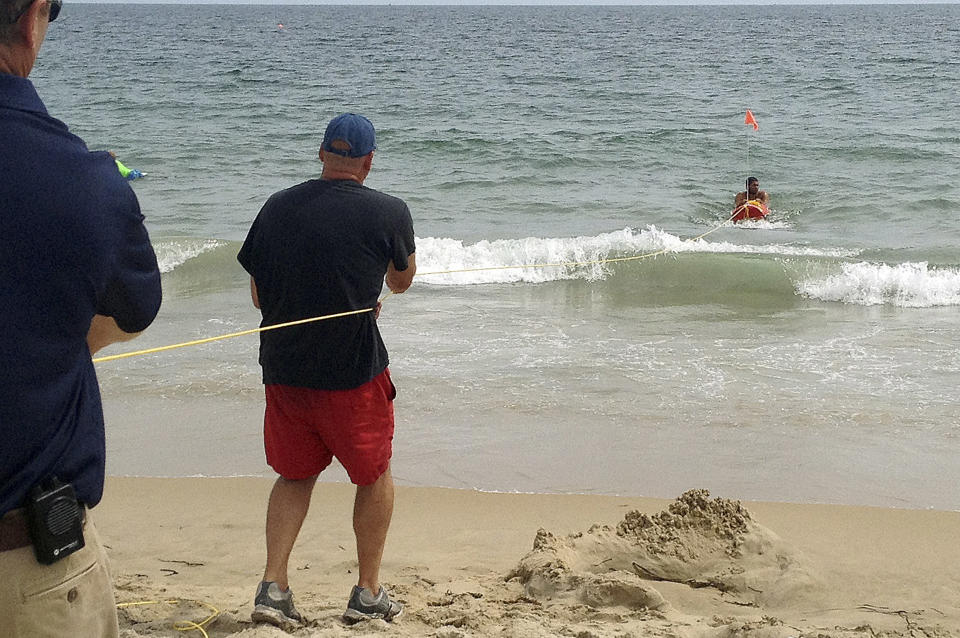 In this Wednesday, Aug, 8, 2012 photo, Misquamicut, R.I., Fire Chief Louis Misto, far left, and lifeguard Jeff Lenihan, center, demonstrate a rescue technique with the EMILY remote-control lifesaving device as lifeguard Philip Campo, in water at right, holds on to the apparatus at Old Town Beach, in Westerly, R.I. EMILY is an acronym for Emergency Integrated Lifesaving Lanyard. (AP Photo/Michelle R. Smith)