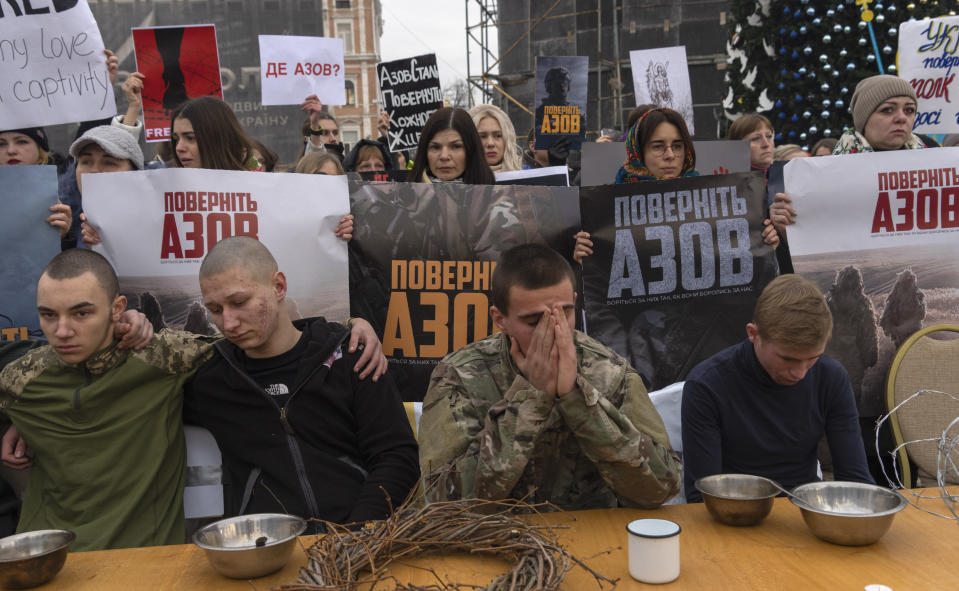 Fellow-in-arms of soldiers from the Azov Regiment, who were captured by Russia in May after the fall of Mariupol, demand to free them at a prison-style Christmas table during a flashmob action in Kyiv, Ukraine, Saturday, Dec. 24, 2022. Relatives of Azove soldiers hold posters reading "Bring Azove back". (AP Photo/Efrem Lukatsky)