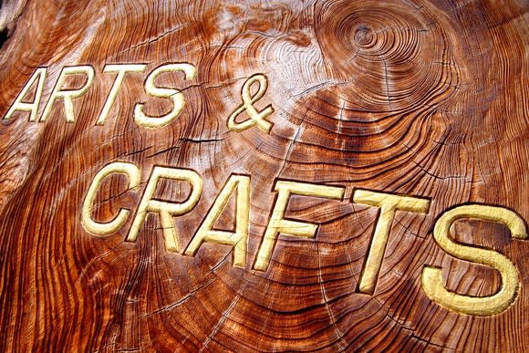 Arts and crafts written in gold on a roughly hewn piece of wood.