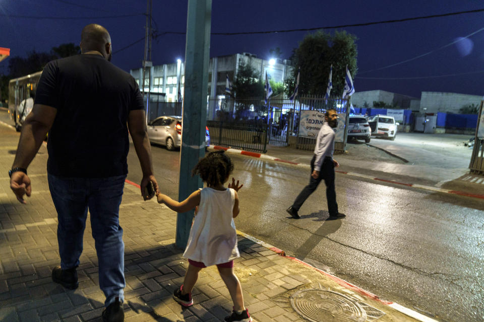 An Arab man walks with a child as Jewish man crosses the street to a Torah Nucleus school in the mixed Arab-Jewish town of Lod, central Israel, Sunday, May 30, 2021. Israel and Hamas reached a truce two weeks ago to end 11 days of fighting in the Gaza Strip. But the roots of the upheavals that wracked Israel's mixed Jewish-Arab cities during the war have not been addressed, leaving those communities on edge. (AP Photo/David Goldman)