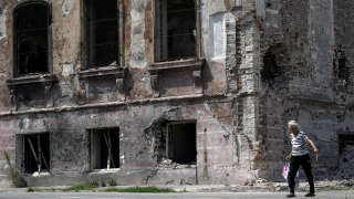 An elderly woman walks past a destroyed building in the city of Mariupol on August 1, 2022, amid the ongoing Russian military action in Ukraine. (Photo by STRINGER / AFP)