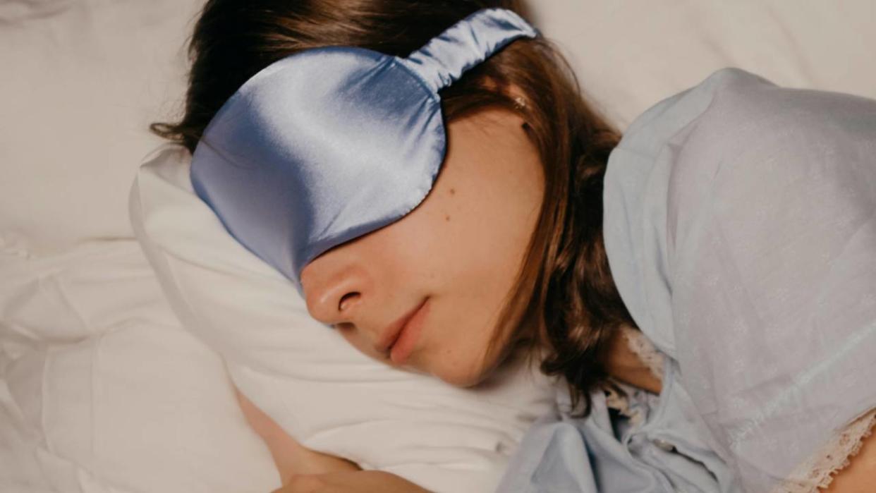  A woman sleeping on her side wearing a blue sleep mask. 