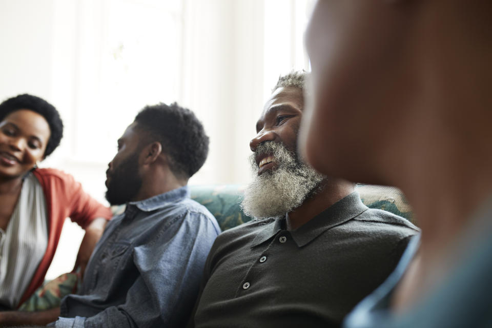 Three people engaged in a relaxed conversation indoors, focus on an older man