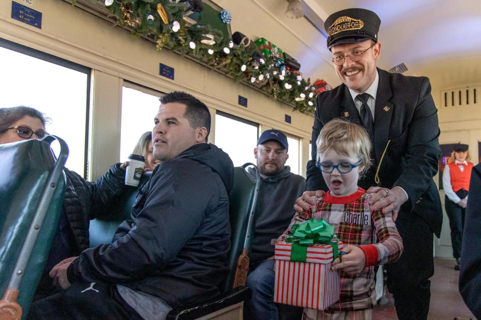 Charlie McClendon walks with the Conductor carrying a present from Santa on "The Polar Express Train Ride" on Christmas Eve in 2022.