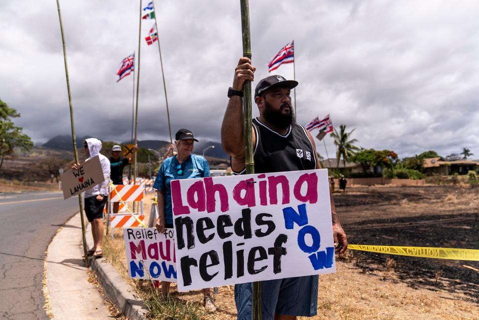 Dustin Pilialoha stands with a sign while waiting for the arrival of President Joe Biden outside the Lahaina Civic Center in Lahaina, Hawaii, on Aug. 21, 2023.