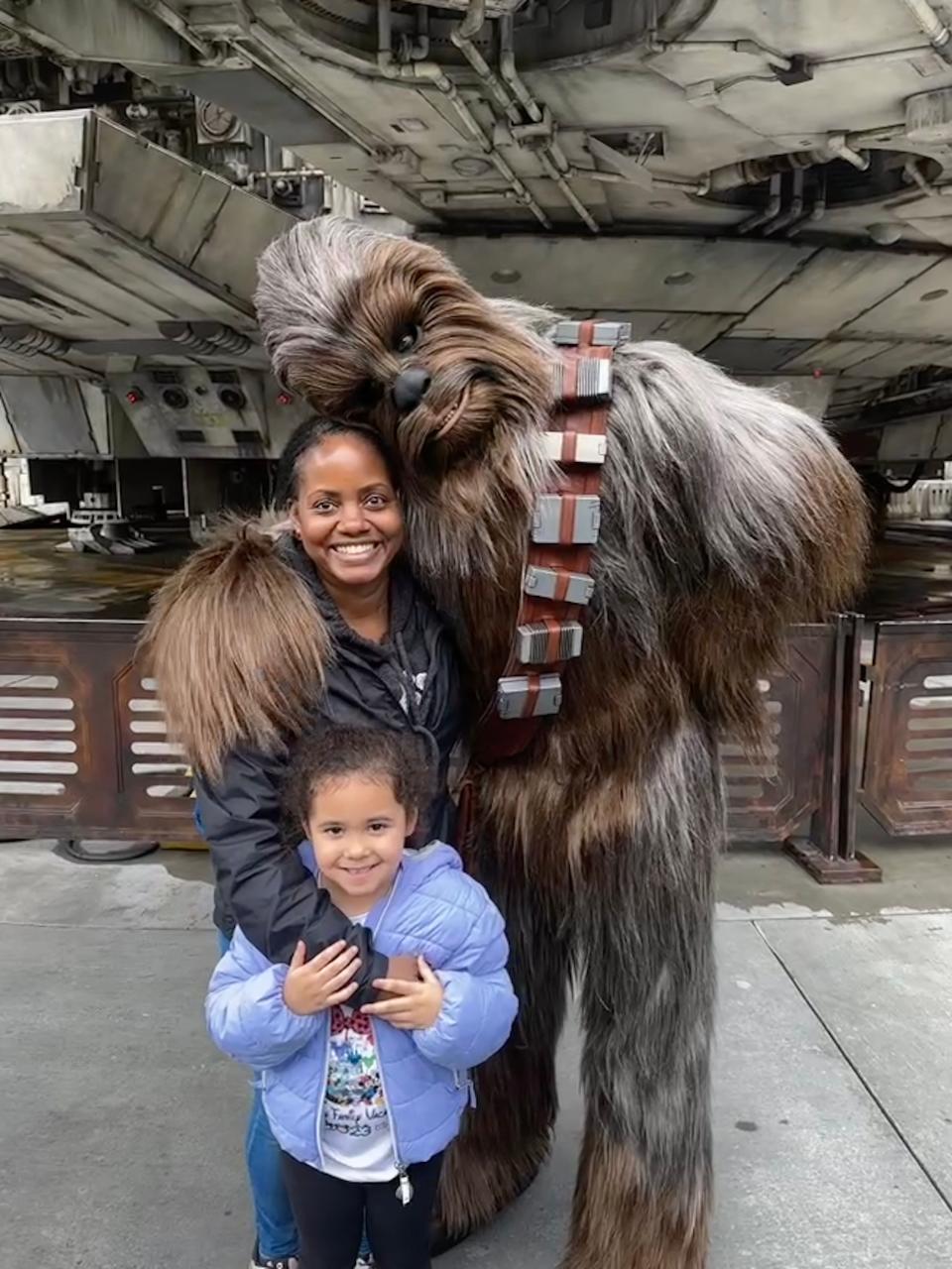 Kelva Stroud-Cooper and her daughter smile alongside Chewbacca at Star Wars: Galaxy's Edge in Disneyland.