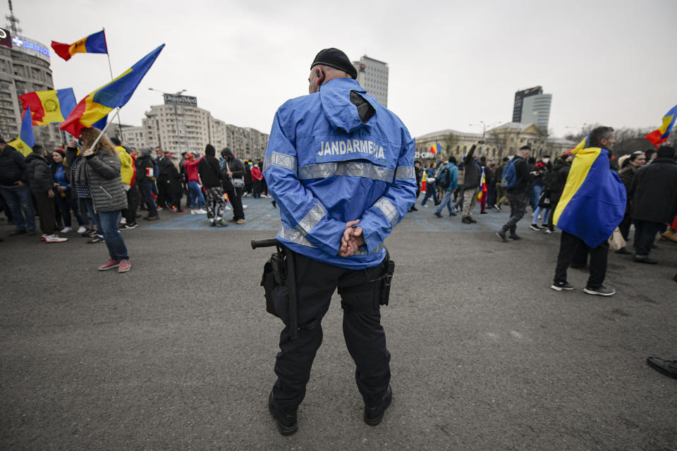 A riot policeman stands as people arrive outside the government headquarters during a protest against the COVID-19 pandemic restrictions in Bucharest, Romania, Saturday, April 3, 2021. Anti-restriction protesters have taken to the streets in several Romanian cities against new pandemic measures that came into force a day earlier amid rising COVID-19 infections. More than a thousand people gathered in the capital of Bucharest. (AP Photo/Andreea Alexandru)