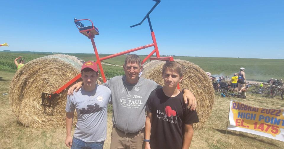 Camric, left, Lance, center, and Kael Hamann in front of a bike sculpture that helped draw thousands of riders to a fundraiser on their farm Sunday, the first day of RAGBRAI 2022.