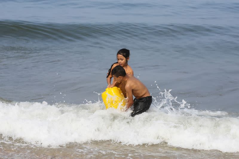 Niños palestinos llenan un recipiente con agua de mar que utilizan para lavar ropa y artículos de cocina, en medio de la falta de agua potable, mientras continúa el conflicto entre Hamás e Israel, en una playa de Deir al-Balah, en el centro de la Franja de Gaza