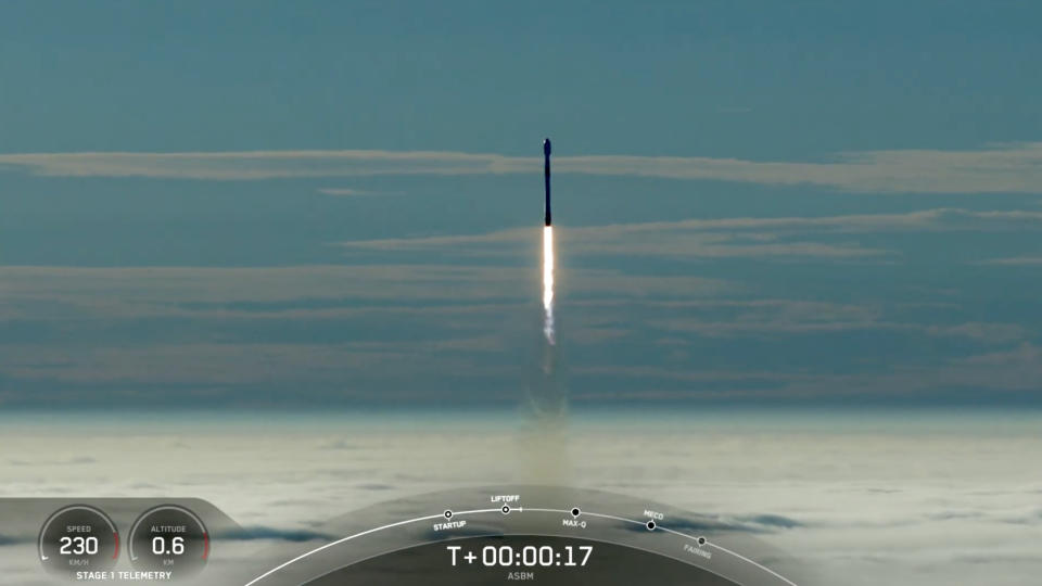  A black-and-white spacex falcon 9 rocket launches into a blue sky, rising above a blanket of fog. 