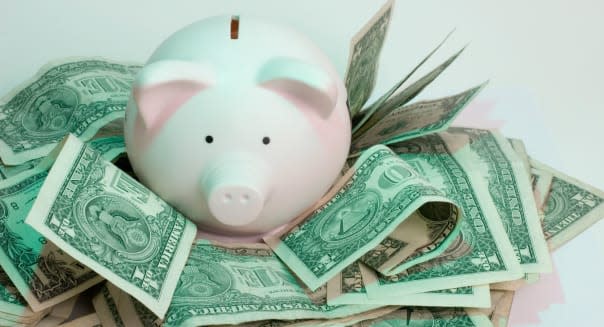A Pink Piggy Bank Surrounded by US Dollars against a white background