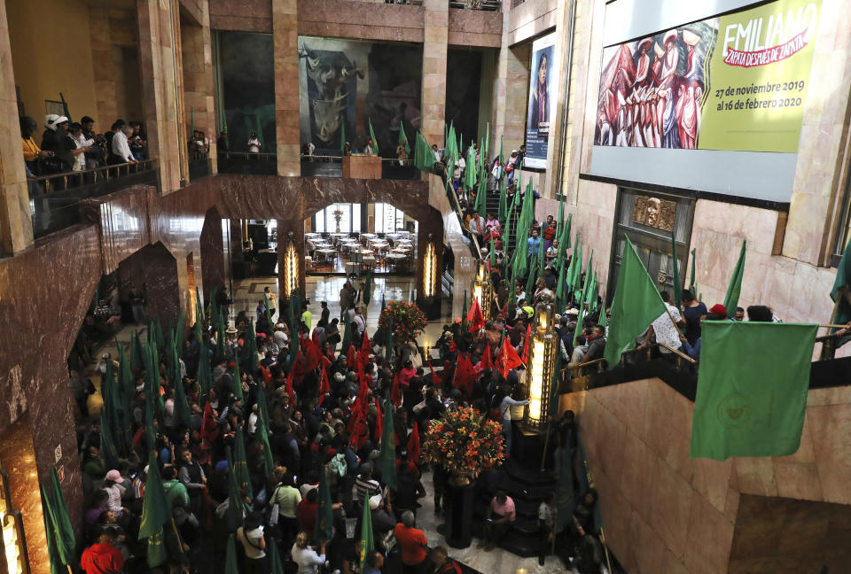 Farm workers block the entrance of the Fine Arts Palace to protest against a painting showing 1910-17 Mexican revolutionary hero Emiliano Zapata nude, wearing high heels and a pink, broad-brimmed hat, straddling a horse, in Mexico City, Tuesday, Dec. 10, 2019. The work by Fabian Chairez is part of an exhibit about Zapata in one of Mexico City's premiere arts venues, the Fine Arts Palace. (AP Photo/Eduardo Verdugo)