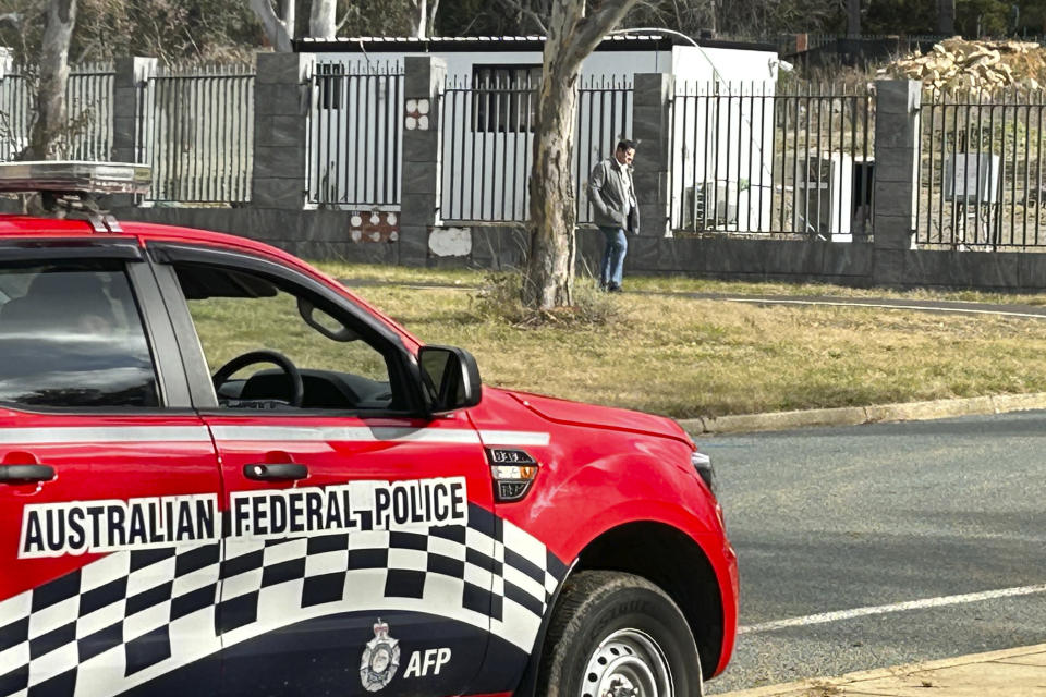 A man walks along a fence that surrounds a a building on the grounds of a proposed new Russian embassy near the Australian Parliament in Canberra where an Australian Federal Police officer observes from his vehicle, Friday, June 23, 2023. A suspected lone Russian diplomat is apparently squatting on the site of the proposed embassy that the Australian government has vetoed. Australian Prime Minister Anthony Albanese dismissed the Russian act of defiance saying a "bloke standing in the cold on a bit of grass in Canberra is not a threat to our national security." (AP Photo/Rod McGuirk)