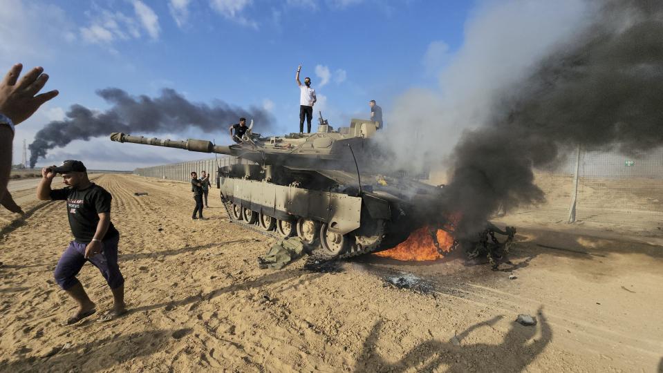 Palestinians celebrate by a destroyed Israeli tank at the Gaza Strip fence east of Khan Younis on Saturday, Oct. 7, 2023. The militant Hamas rulers of the Gaza Strip carried out an unprecedented, multi-front attack on Israel at daybreak Saturday, firing thousands of rockets as dozens of Hamas fighters infiltrated the heavily fortified border in several locations by air, land, and sea and catching the country off-guard on a major holiday.