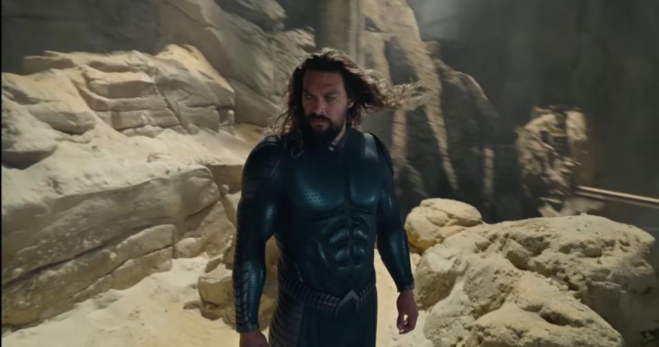 A bearded man in an all-black suit examines a sandy mountain formation