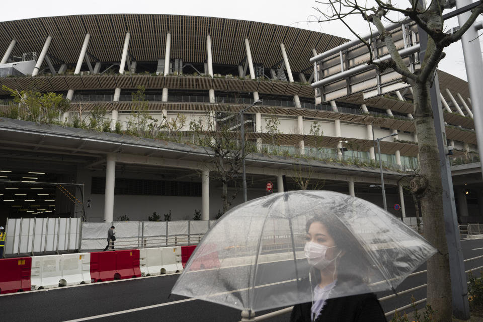 A woman walks past the New National Stadium, a venue for the opening and closing ceremonies at the Tokyo 2020 Olympics, in Tokyo, Monday, March 23, 2020. The IOC will take up to four weeks to consider postponing the Tokyo Olympics amid mounting criticism of its handling of the coronavirus crisis that now includes a call for delay from the leader of track and field, the biggest sport at the games. (AP Photo/Jae C. Hong)