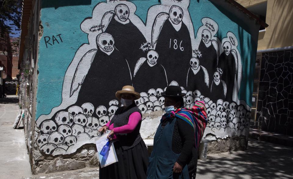 En esta imagen de archivo, tomada el 23 de septiembre de 2020, dos mujeres pasan por delante de un mural que simboliza la muerte de camino a la tumba de un familiar fallecido por complicaciones relacionadas con el coronavirus, en el Cementerio General, en La Paz, Bolivia. Los bolivianos enfrentan otro episodio con un gobierno débil, volatilidad política y problemas económicos en un momento en que la pandemia del coronavirus y las cuarentenas decretadas para frenarla están acabando con años de avances para aliviar la pobreza. (AP Foto/Juan Karita, archivo)