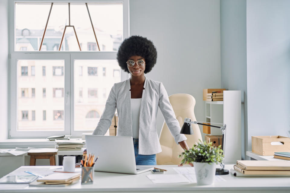 Attractive young African woman leaning at the office desk and looking at camera