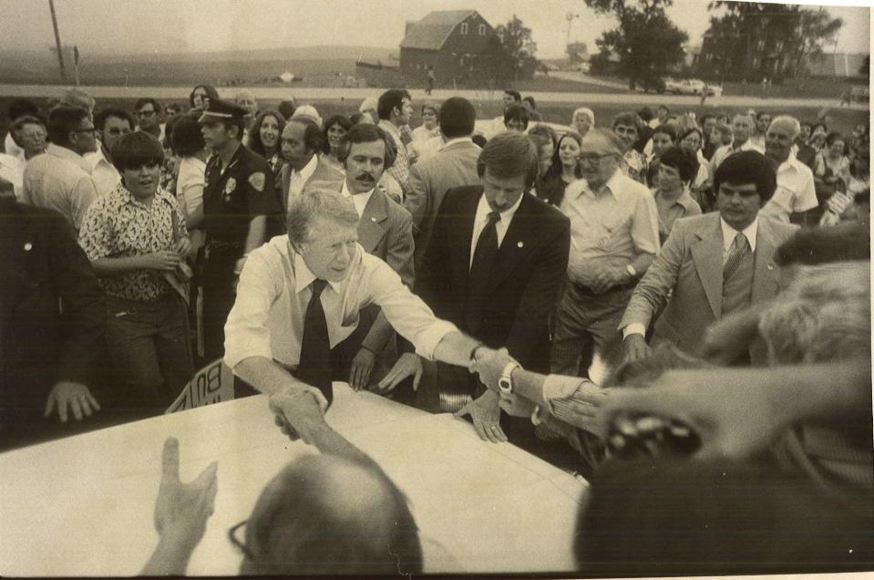 With at least four secret servicemen and one uniformed policeman surrounding him, Democratic presidential candidate Jimmy Carter reaches out with both hands to greet well-wishers who crowded into a Warren County farm pasture on Aug. 25, 1976. Each person paid $10 to get in.