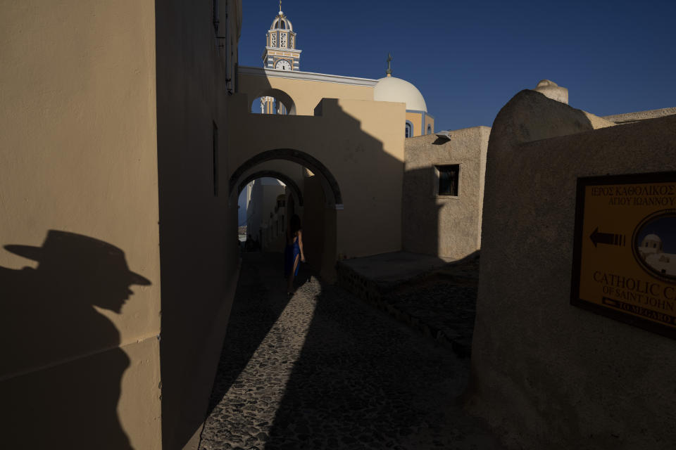 A woman poses in an alley between the Cathedral of St. John the Baptist, right, and the Monastery of St. Catherine on the Greek island of Santorini on Wednesday, June 15, 2022. Inside the convent, 13 cloistered nuns devote their lives to prayer. (AP Photo/Petros Giannakouris)