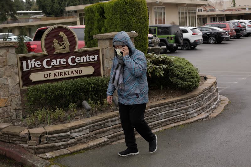 A woman walks out of Life Care Center of Kirkland as an ambulance transports a patient from the long-term care facility, which is linked to the two of three confirmed coronavirus cases in the state, in Kirkland