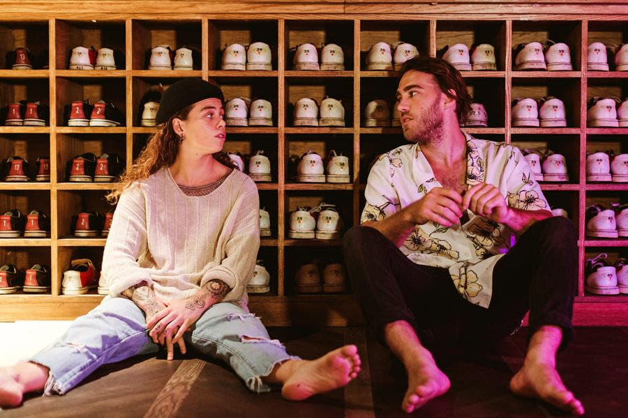 Australian singers Matt Corby and Tash Sultana sit in front of bowling shoes. 