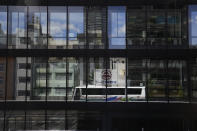 A bus carrying members of the media is reflected on glass windows of a building ahead of the 2020 Summer Olympics, Friday, July 16, 2021, in Tokyo. The pandemic-delayed games open on July 23 without spectators at most venues. (AP Photo/Jae C. Hong)