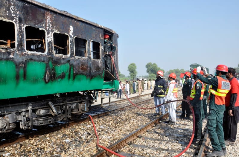 Firefighters and rescue workers gather near the place where a fire broke out in a passenger train and destroyed three carriages near the town of Rahim Yar Khan