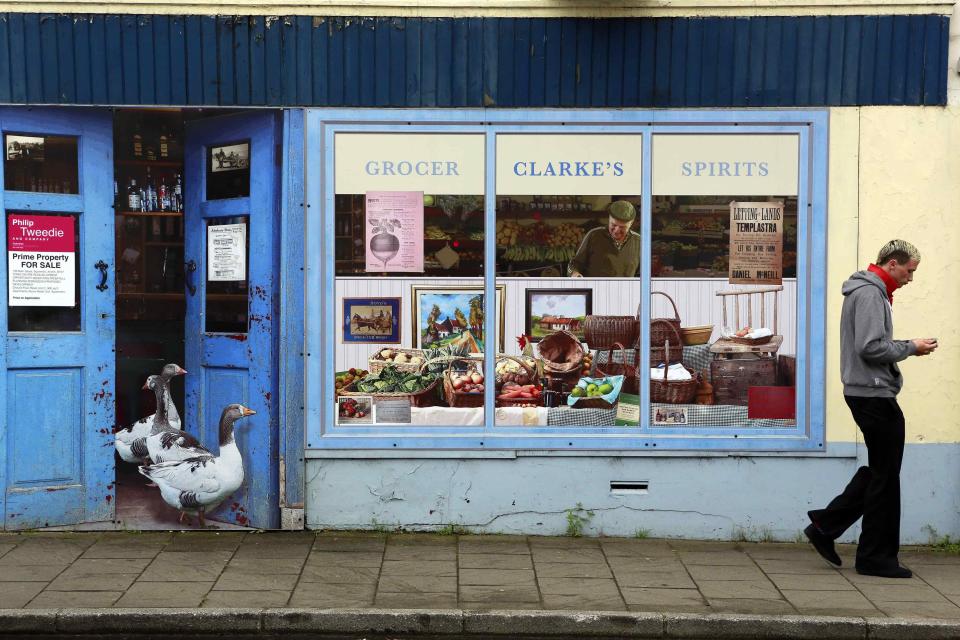 Man walks past an empty shop, which has been covered with artwork to make it look more appealing, in the village of Bushmills on the Causeway Coast