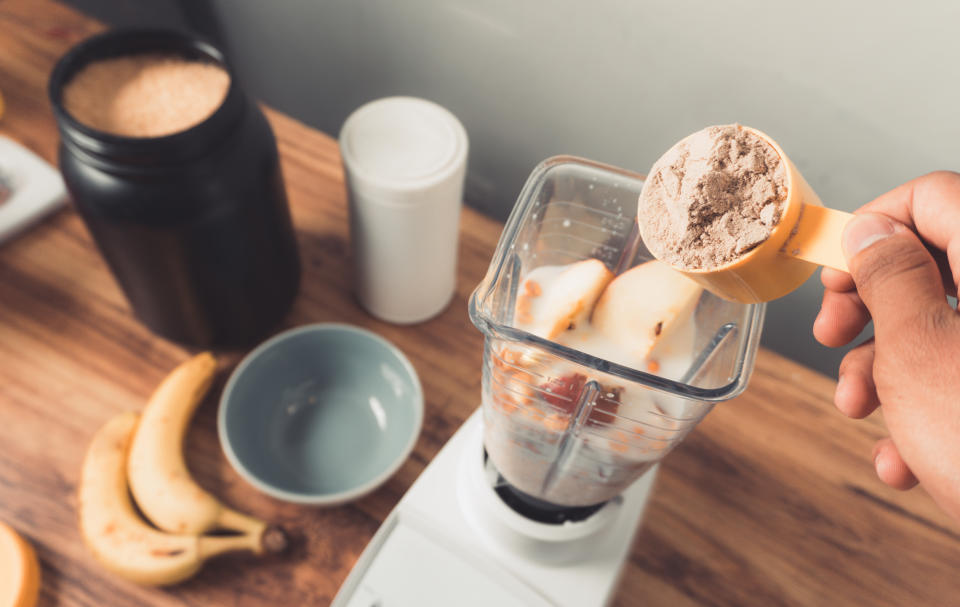 Hand holding a protein scoop over blender with smoothie.