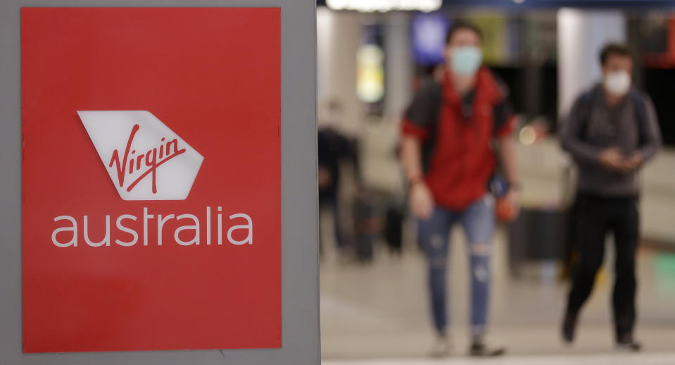 Passengers walk past a Virgin Australia sign at Sydney Airport in Sydney, Wednesday, Aug. 5, 2020. Virgin Australia will cut about 3000 jobs as the airline struggles with the effects of the coronavirus pandemic. (AP Photo/Rick Rycroft)