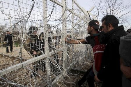 Refugees and migrants stand next to a border fence at the Greek-Macedonian border, after Macedonia closed its borders with Greece for Afghan migrants and demands additional identification from people seeking to cross the border and head to Western Europe, near the village of Idomeni, Greece, February 22, 2016. REUTERS/Alexandros Avramidis