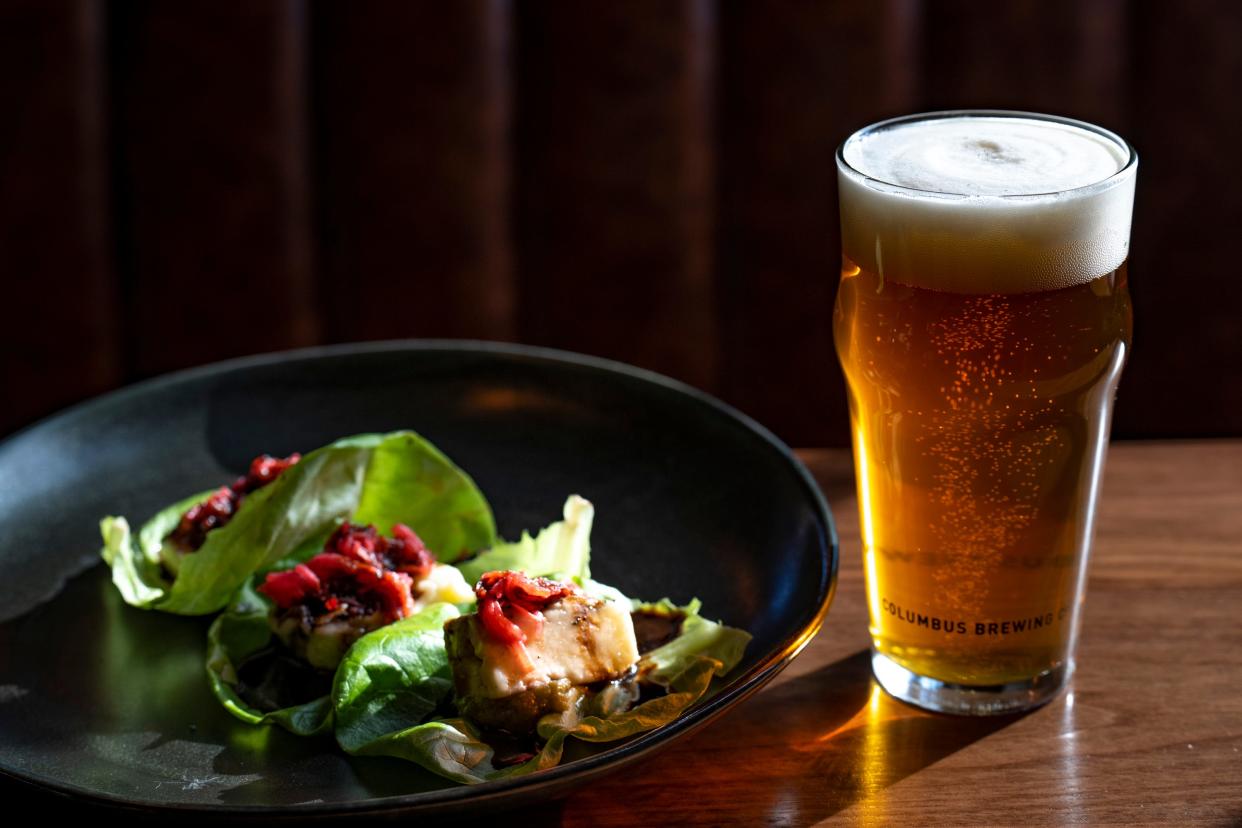 A Calhoun pale ale rests on a tabletop next to halloumi lettuce cups at Columbus Brewing Company’s newly opened beer hall in Franklin Park.